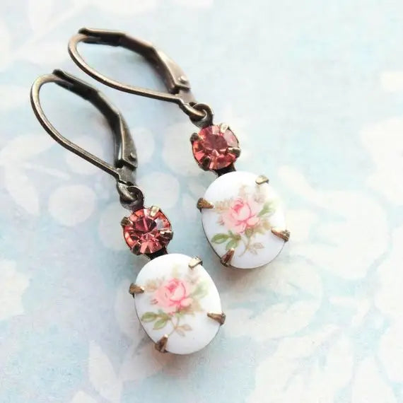 Pair of earrings with floral designs and pink gemstones on a light blue background