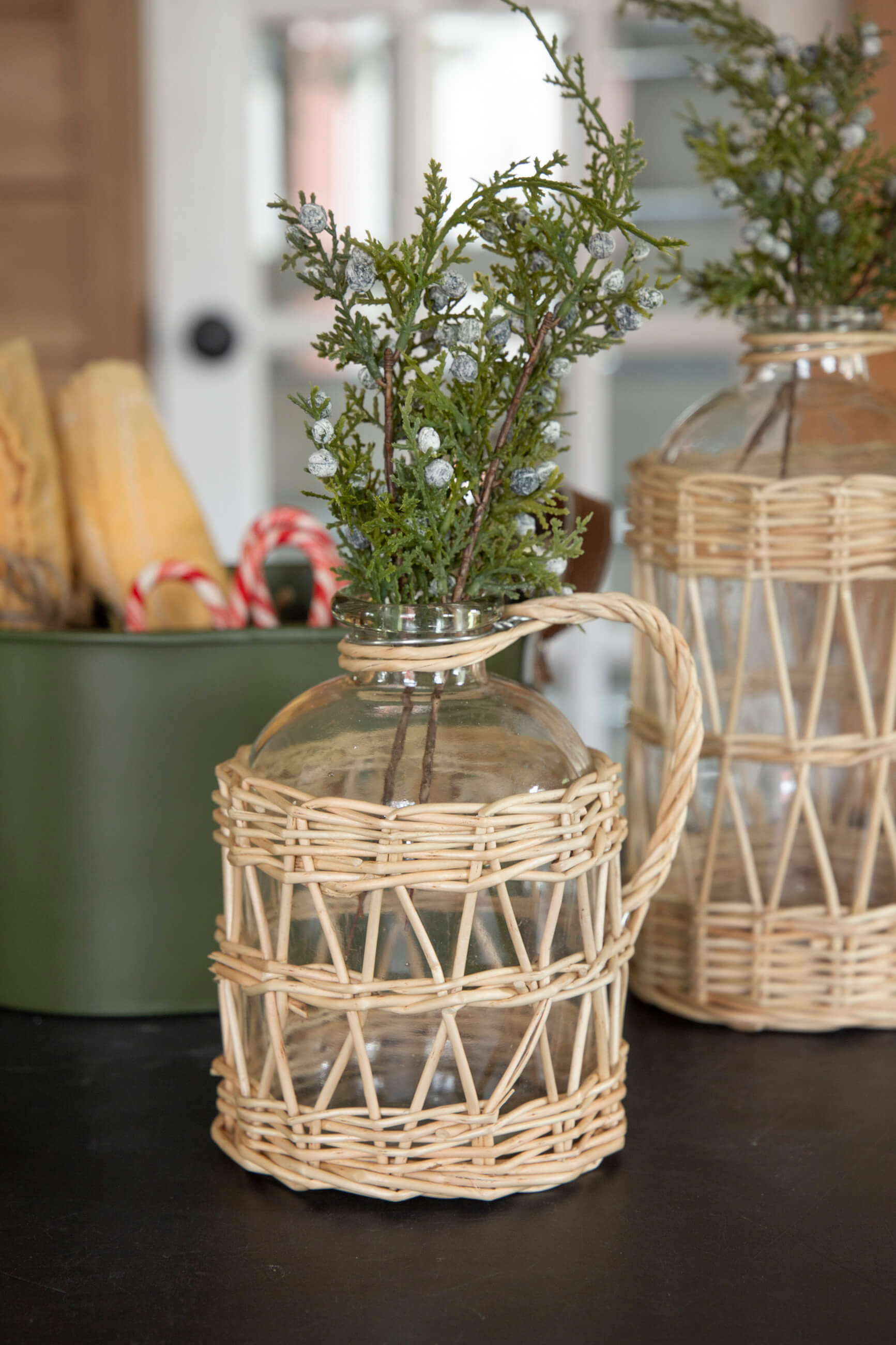 Decorative glass container with wicker basket on a dark surface, with another similar container in the background.