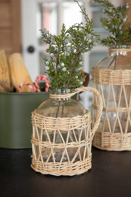 Decorative glass container with wicker basket on a dark surface, with another similar container in the background.